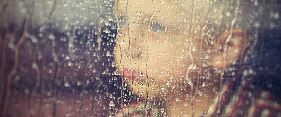 Young boy looking out window on rainy day