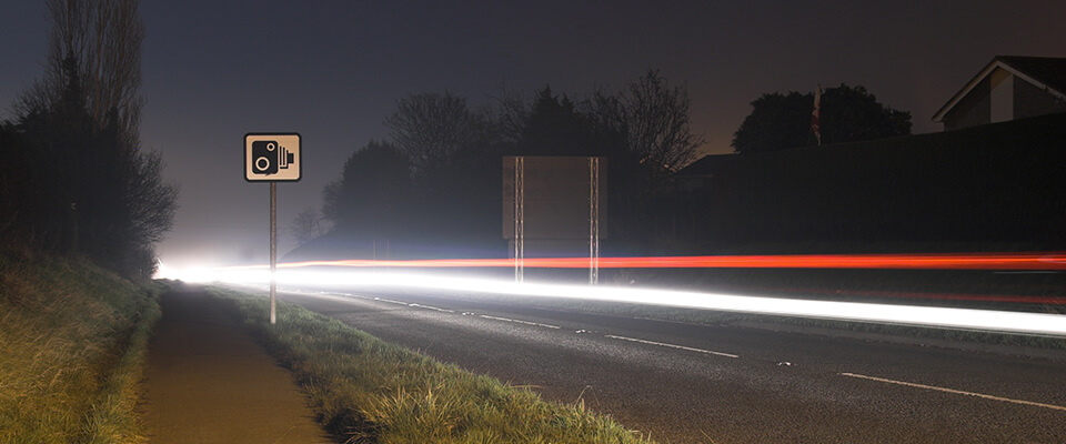 Long exposure speeding car lights with speed camera sign